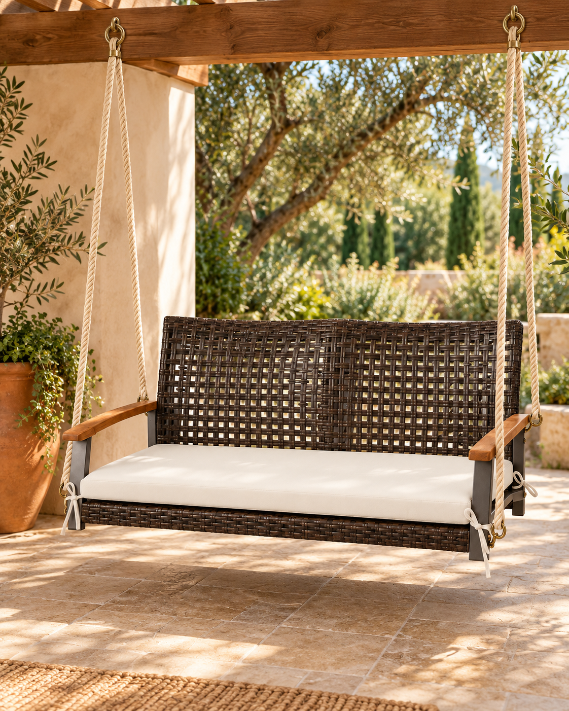 Balancelle suspendue en résine tressée brune avec coussin écru sous une pergola Image