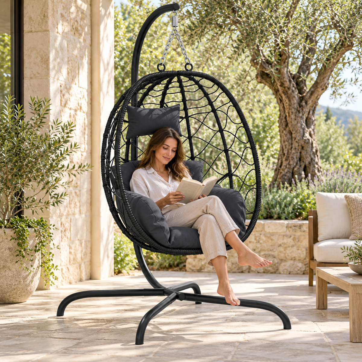 Fauteuil œuf noir sur pied avec coussins anthracite avec une personne sur une terrasse
