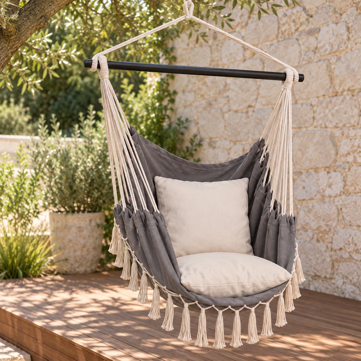 Chaise hamac grise à franges et coussins écrus, vue de trois quarts sur une terrasse